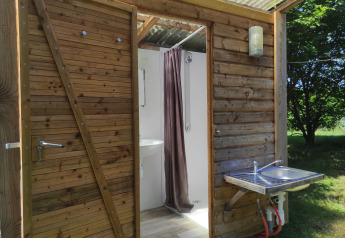 Outdoor wooden bathroom with open door and sink at Safari Greenlodge, Camping Domaine La Chabanne, France.