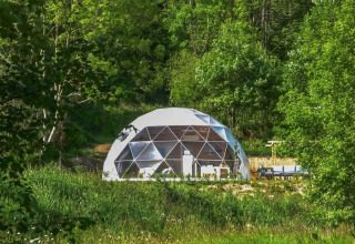 Geodesic dome at Camping Domaine La Chabanne, France, nestled in lush greenery and surrounded by trees.