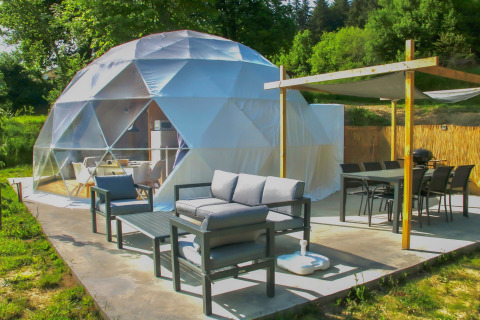 Udendørs opholdsområde ved Dome på Camping Domaine La Chabanne i Frankrig med moderne møbler og grønne omgivelser.
