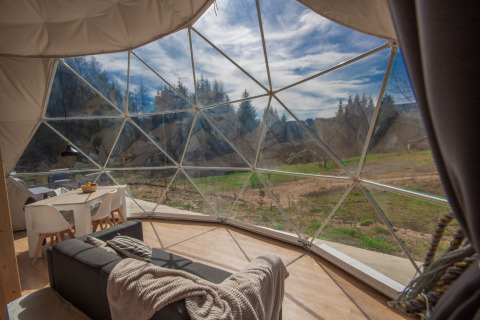 Vista interior de una cúpula en Camping Domaine La Chabanne en Francia con paredes de vidrio y paisaje natural.