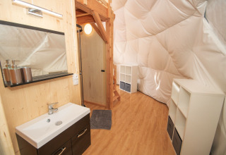 Interior of Dome at Camping Domaine La Chabanne, France, featuring sink, staircase, white shelves and wood floor.