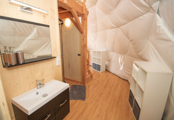 Interno della Cupola al Camping Domaine La Chabanne, Francia, con lavabo, scale in legno e scaffali bianchi.