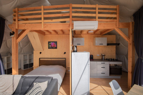 Vista interior de una cúpula en Camping Domaine La Chabanne, Francia, con entrepiso y cocina moderna.