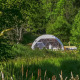 Un Domo geodésico rodeado de vegetación y árboles, capturado en un día soleado en medio del bosque.