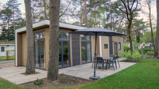 Lodge moderne Cube la Mer à De Zanding aux Pays-Bas, entouré d’arbres et d’une terrasse extérieure.