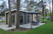 Moderne lodge kaldet Cube la Mer ved De Zanding i Holland, omgivet af træer og have med terrasse.