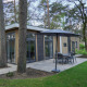 Moderne lodge Cube la Mer in De Zanding, Nederland, omringd door bomen en een terras met tuinmeubilair.