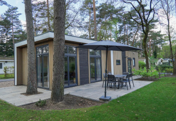 Lodge moderne Cube la Mer à De Zanding aux Pays-Bas, entouré d’arbres et d’une terrasse extérieure.