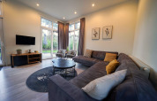 Modernes Wohnzimmer mit Ecksofa, Rundtischen und großen Fenstern in Cube la Mer, De Zanding, Niederlande.