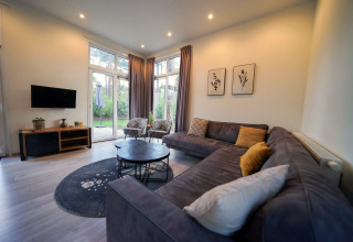 Modern living room with large sectional, round tables, and big windows at Cube la Mer, De Zanding, Netherlands.