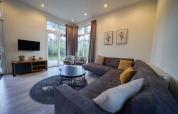 Modernes Wohnzimmer mit Ecksofa, Rundtischen und großen Fenstern in Cube la Mer, De Zanding, Niederlande.