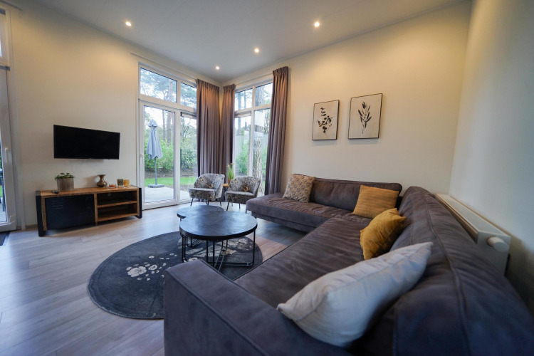 Modernes Wohnzimmer mit Ecksofa, Rundtischen und großen Fenstern in Cube la Mer, De Zanding, Niederlande.