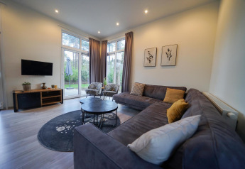 Moderne leefruimte met grote hoekzetel, ronde tafels en grote ramen in Cube la Mer, De Zanding, Nederland.