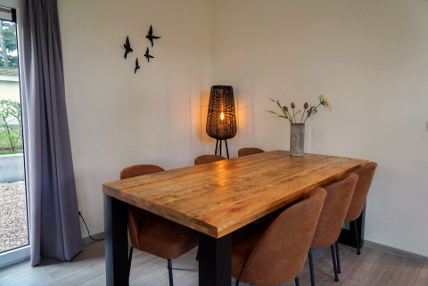 Dining area in Cube la Mer at De Zanding, Netherlands, with wooden table, six chairs, lamp, and wall art.