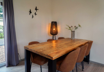 Comedor en Cube la Mer en De Zanding, Países Bajos, con mesa de madera, seis sillas, lámpara y decoración mural.