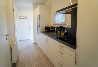 Cucina moderna e compatta presso Cube la Mer a De Zanding, Paesi Bassi, con mobili bianchi e piano nero.