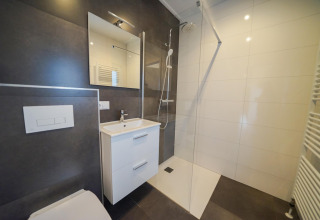 Baño moderno con ducha, lavabo con cajones y espejo en Cube la Mer, De Zanding, Países Bajos.