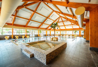 Piscina cubierta en una cabaña con techo de madera moderno, zona de spa y asientos cómodos.