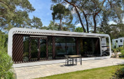 Lodge moderno Mode Sauna en De Zanding, Países Bajos, rodeado de árboles y patio con muebles exteriores.