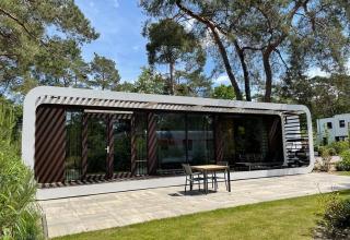 Lodge moderno Mode Sauna en De Zanding, Países Bajos, rodeado de árboles y patio con muebles exteriores.