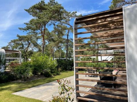 Außenbereich der Mode Sauna-Lodge bei De Zanding, Niederlande, mit Holzterrasse und umgebenden Bäumen.