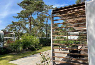 Außenbereich der Mode Sauna-Lodge bei De Zanding, Niederlande, mit Holzterrasse und umgebenden Bäumen.