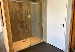 Moderne douche met glazen deuren naast een witte deur bij Mode Sauna, De Zanding, Nederland.