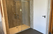 Moderne brusekabine med glasdøre og regnbruser, ved siden af en hvid dør i Mode Sauna, De Zanding.