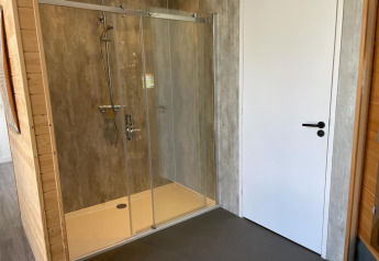 Moderne brusekabine med glasdøre og regnbruser, ved siden af en hvid dør i Mode Sauna, De Zanding.
