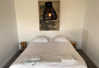 Slaapkamer in Mode Sauna bij De Zanding, Nederland, met tweepersoonsbed, lampen en wanddecoratie.