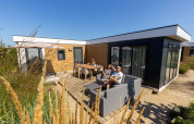 Familia relajándose al aire libre en Zonneweelde Lodge XL en Camping Zonneweelde, Países Bajos, en un día soleado.
