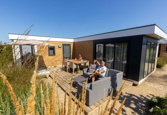 Famiglia che si rilassa all'esterno di Zonneweelde Lodge XL al Camping Zonneweelde nei Paesi Bassi in una giornata soleggiata.