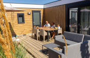Gezin ontspant op het terras van Zonneweelde Lodge XL bij Camping Zonneweelde in Nederland op een zonnige dag.