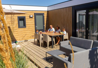 Gezin ontspant op het terras van Zonneweelde Lodge XL bij Camping Zonneweelde in Nederland op een zonnige dag.