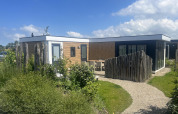 Buitenaanzicht van de Zonneweelde Lodge XL bij Camping Zonneweelde in Nederland, omringd door natuur.
