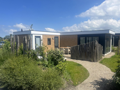Udsigt til Zonneweelde Lodge XL ved Camping Zonneweelde i Holland, moderne lodge omgivet af grønt.