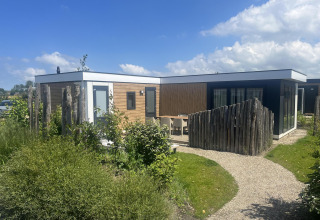 Udsigt til Zonneweelde Lodge XL ved Camping Zonneweelde i Holland, moderne lodge omgivet af grønt.