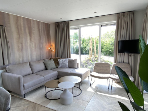 Moderne stue i Zonneweelde Lodge XL på Camping Zonneweelde i Holland, med sofa, stole og store vinduer.
