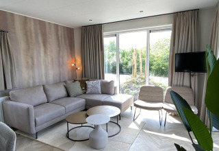 Moderne stue i Zonneweelde Lodge XL på Camping Zonneweelde i Holland, med sofa, stole og store vinduer.