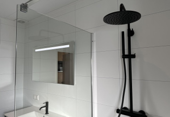 Bagno moderno con doccia nera, lavabo e specchio nella Zonneweelde Lodge XL, Camping Zonneweelde, Paesi Bassi.