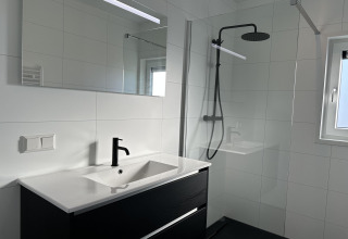 Baño moderno con grifo negro, gran espejo y ducha a ras de suelo en Zonneweelde Lodge XL, Países Bajos.