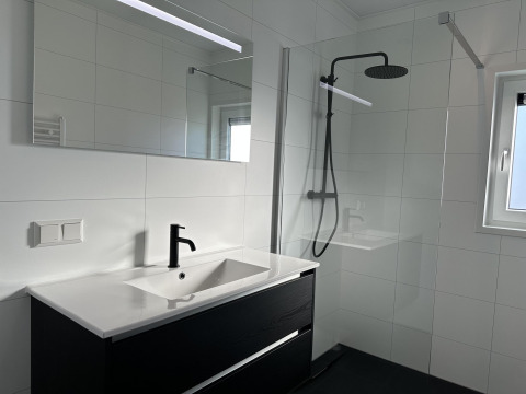 Baño moderno con grifo negro, gran espejo y ducha a ras de suelo en Zonneweelde Lodge XL, Países Bajos.