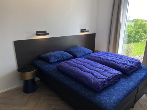 Chambre moderne avec lit double et draps bleus à Zonneweelde Lodge XL, Camping Zonneweelde, aux Pays-Bas.