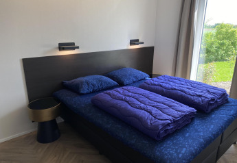 Camera moderna con letto matrimoniale e biancheria blu nella Zonneweelde Lodge XL, Camping Zonneweelde, Olanda.