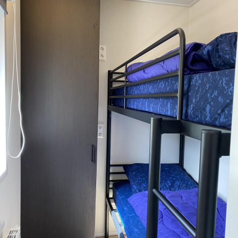 Petite chambre avec lit superposé et porte en bois foncé à la Zonneweelde Lodge XL, Camping Zonneweelde, Pays-Bas.
