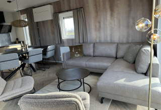 Sala moderna y acogedora en Zonneweelde Lodge XL en Camping Zonneweelde, Países Bajos, con muebles grises.