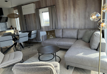 Moderne living in Zonneweelde Lodge XL op Camping Zonneweelde, Nederland, met grijze meubels en gezellige sfeer.