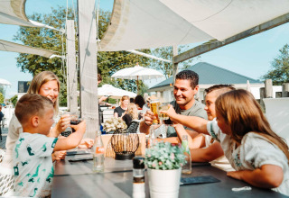Gezin proost samen en geniet van een lunch buiten aan Zonneweelde Lodge XL op Camping Zonneweelde, Nederland.