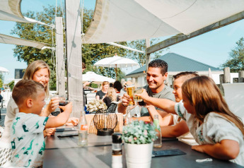 Famiglia che brinda e pranza all’aperto presso Zonneweelde Lodge XL, Camping Zonneweelde, nei Paesi Bassi.