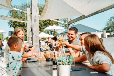 Familie nyder en udendørs frokost og skåler sammen på Zonneweelde Lodge XL, Camping Zonneweelde, Nederlandene.